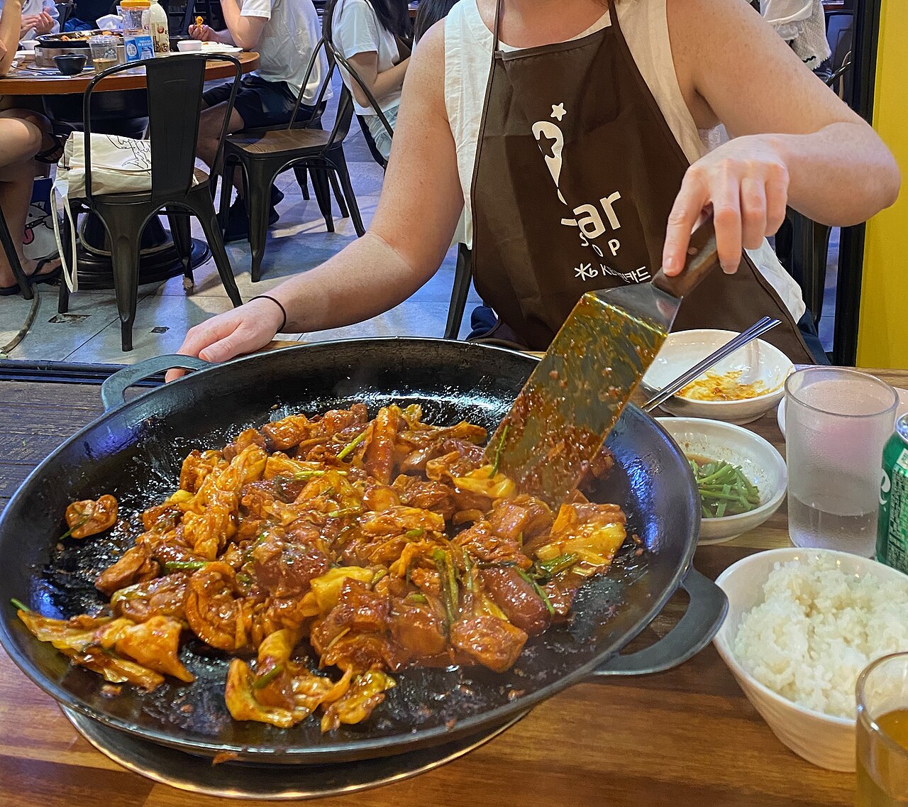 Diner stirring dakgalbi with a spatula on a large iron plate at a Seoul restaurant