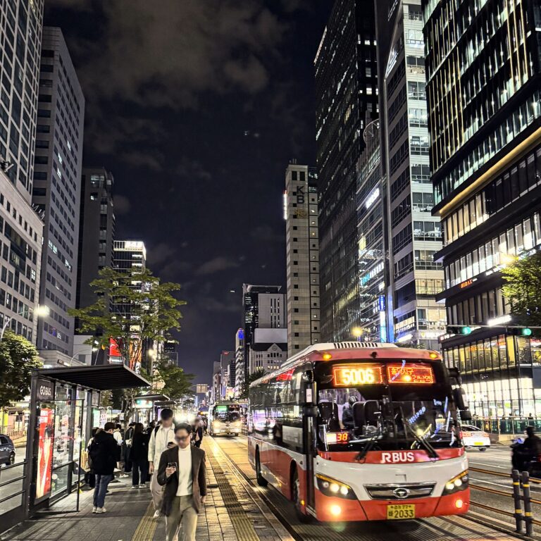 Gangnam Station area at night with a city bus, office towers and commuters in Seoul