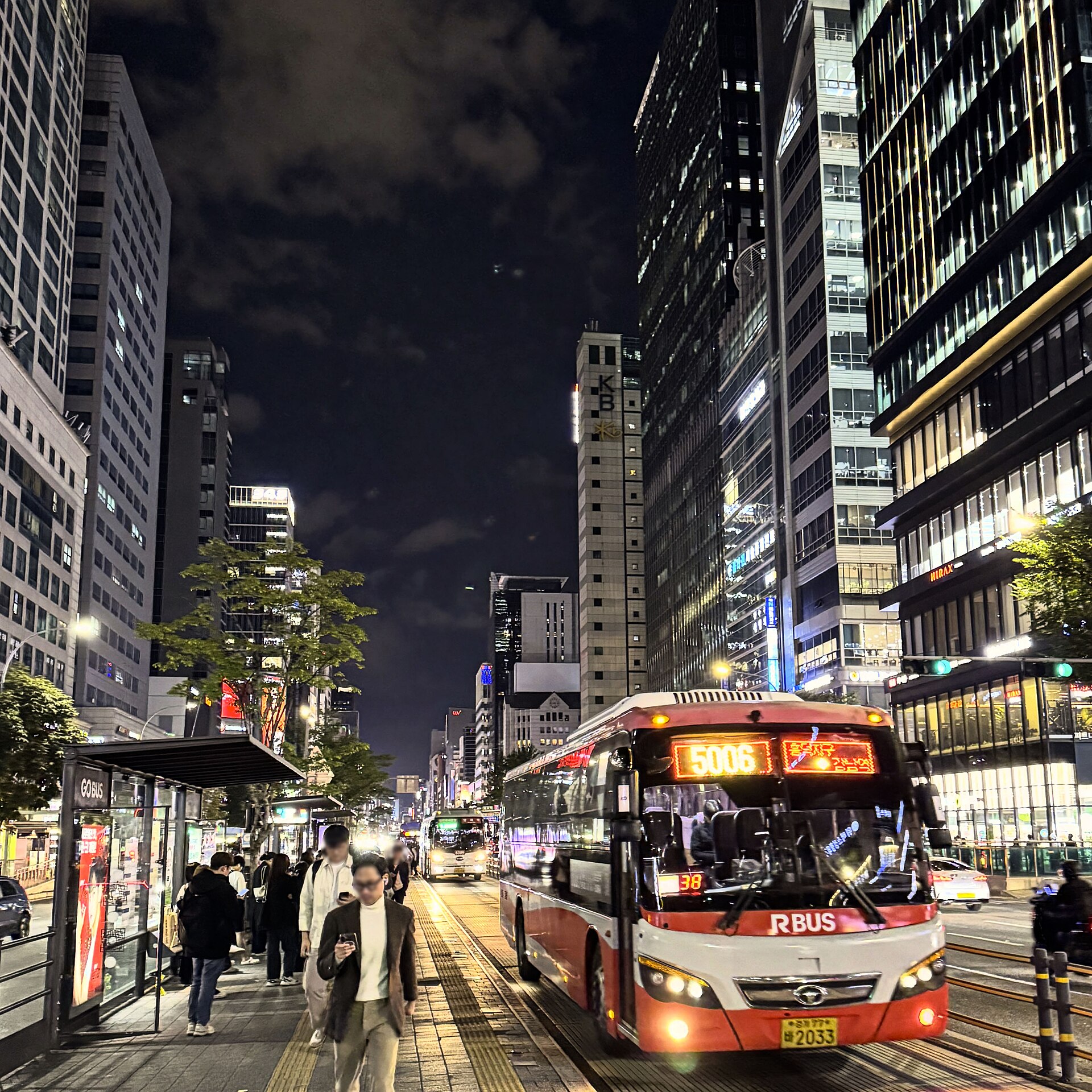Gangnam Station area at night with a city bus, office towers and commuters in Seoul